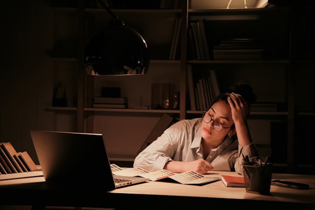 Femme fatiguée, penchée sur un bureau en fin de journée, évoquant le stress chronique et ses effets sur la fertilité.