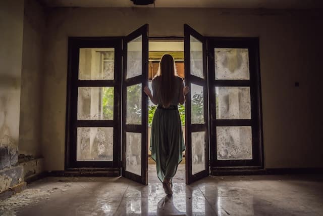 Femme debout face à une fenêtre, lumière naturelle, symbolisant l’attente silencieuse liée à la fertilité